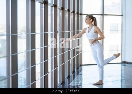 Bella donna in abbigliamento sportivo bianco in sala ginnastica. Ragazza atletica che si riscalda prima di formazione Foto Stock