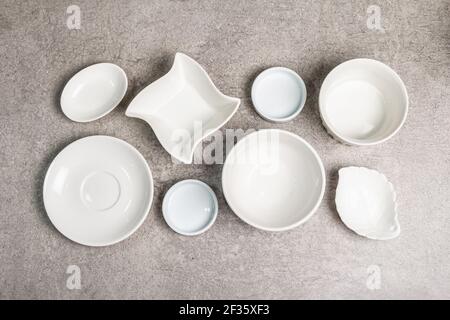 Ciotole vuote e piatti bianchi assortiti su fondo di pietra. Diversi piatti in ceramica e utensili da cucina, vista dall'alto Foto Stock