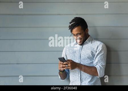 Sorridente giovane hipster nero maschio godere di internet surf su cella Foto Stock
