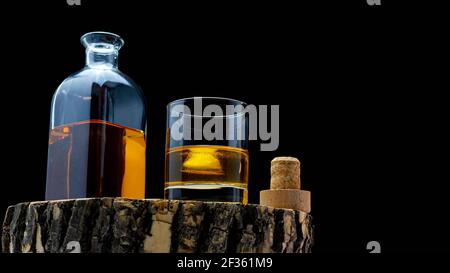 Bottiglia di whisky su un asse di legno con un bicchiere riempito di whisky di ghiaccio su sfondo nero. Foto Stock