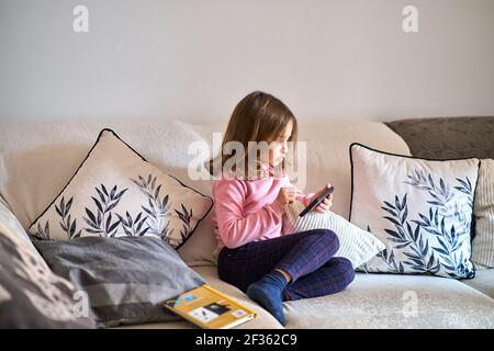 Una bambina seduta su un divano che gioca con un telefono Foto Stock