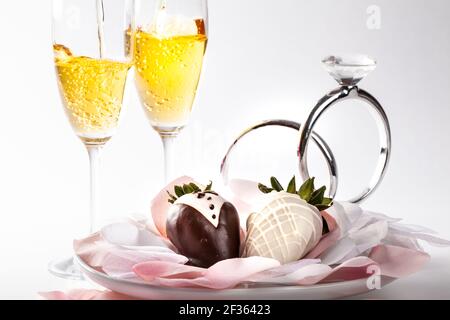 Fragole ricoperte di cioccolato decorate come sposa e sposo con bicchieri di champagne sullo sfondo Foto Stock