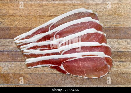 Cinque rashers di pancetta posteriore asciutta-cured non fumata su un marrone tavolo in legno a doghe Foto Stock