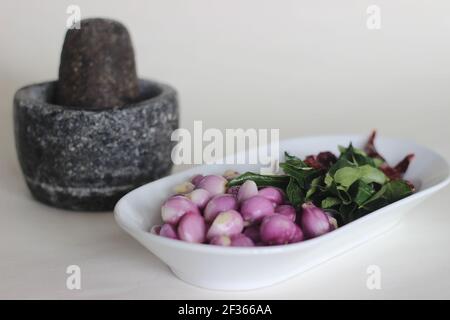 Scalogni, foglie di curry e peperoncini rossi pronti ad essere frapponati con pestello e mortaio. Modo tradizionale di preparare gli ingredienti per il prepar stile Kerala Foto Stock