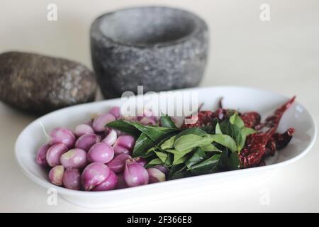 Scalogni, foglie di curry e peperoncini rossi pronti ad essere frapponati con pestello e mortaio. Modo tradizionale di preparare gli ingredienti per il prepar stile Kerala Foto Stock