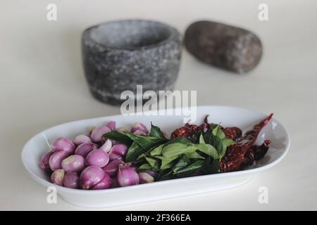 Scalogni, foglie di curry e peperoncini rossi pronti ad essere frapponati con pestello e mortaio. Modo tradizionale di preparare gli ingredienti per il prepar stile Kerala Foto Stock