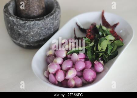 Scalogni, foglie di curry e peperoncini rossi pronti ad essere frapponati con pestello e mortaio. Modo tradizionale di preparare gli ingredienti per il prepar stile Kerala Foto Stock