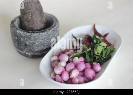 Scalogni, foglie di curry e peperoncini rossi pronti ad essere frapponati con pestello e mortaio. Modo tradizionale di preparare gli ingredienti per il prepar stile Kerala Foto Stock