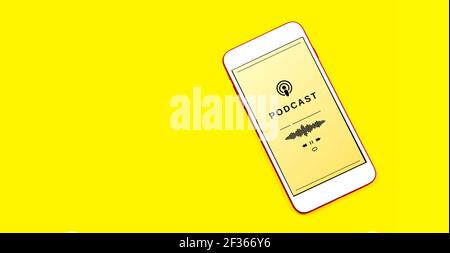 Lo smartphone riproduce un podcast su sfondo giallo. Concetto di ascolto del podcast Foto Stock
