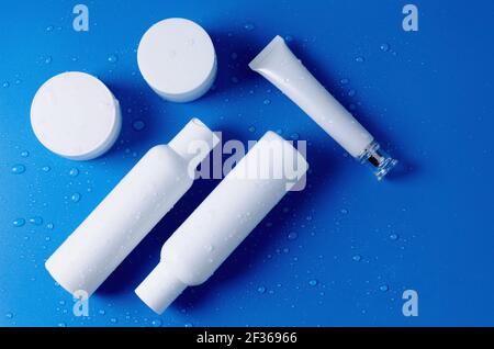Bottiglie cosmetiche bianche, provette, vasetti su sfondo blu con gocce d'acqua. Prodotti cosmetici per la cura della pelle, del corpo, del viso, degli occhi. Vendita prodotti cosmetici te Foto Stock