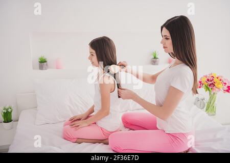 Foto di attraente dolce due fratelli da notte seduta a letto spazzolando i capelli sorridono all'interno della stanza Foto Stock