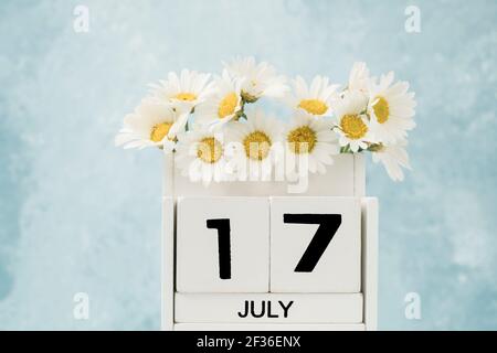 Calendario cubo bianco per luglio decorato con fiori margherita su blu con spazio copia Foto Stock