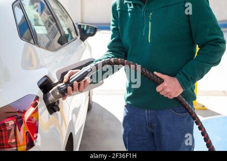 Uomo anziano con maglione verde che si riempie di gas naturale compresso (cng) nella sua auto ecocompatibile. Concetto di energia pulita. Foto Stock