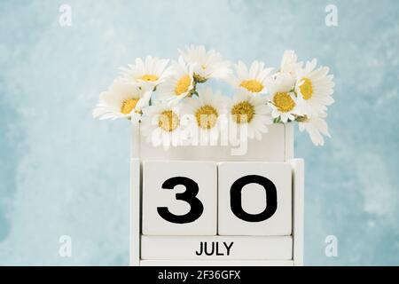 Calendario cubo bianco per luglio decorato con fiori margherita su blu con spazio copia Foto Stock