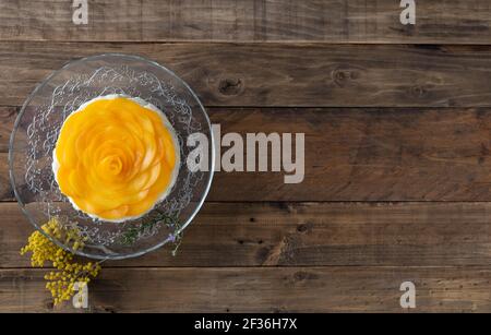 Cheesecake con decorazione di pesca a forma di rosa su fondo di legno. Spazio di copia. Vista dall'alto. Foto Stock