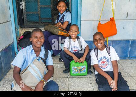 Santo Domingo Repubblica Dominicana, Bajos de Haina Ispanico studenti neri, ragazzi ragazza che indossa uniforme scuola seduta su gradini che tiene pranzo al sacco, Foto Stock