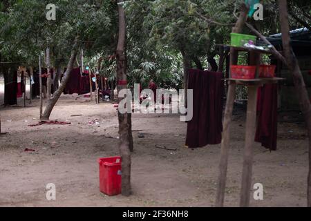 BAGAN, NYAUNG-U, MYANMAR - 2 GENNAIO 2020: Alcuni giovani monaci si siedono sul terreno sterrato in una foresta sdoganata dietro alcuni abiti rossi buddisti appesi Foto Stock