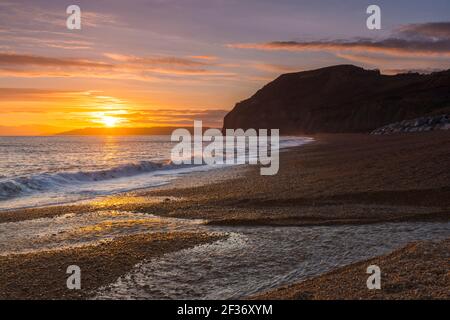 Seatown, Dorset, Regno Unito. 15 marzo 2021. Regno Unito Meteo. Un tramonto spettacolare visto dalla spiaggia che guarda verso le scogliere di Golden Cap a Seatown sulla Dorset Jurassic Coast, come i cieli si stagliano dopo una giornata per lo più sovrastata durante la chiusura del Covid-19. Picture Credit: Graham Hunt/Alamy Live News Foto Stock