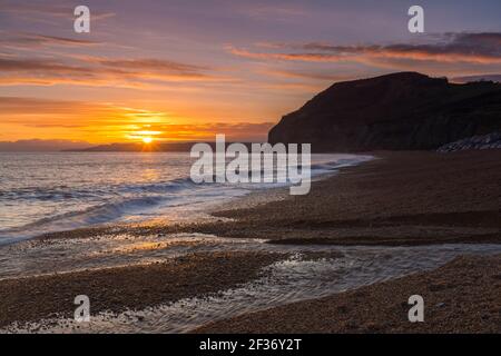 Seatown, Dorset, Regno Unito. 15 marzo 2021. Regno Unito Meteo. Un tramonto spettacolare visto dalla spiaggia che guarda verso le scogliere di Golden Cap a Seatown sulla Dorset Jurassic Coast, come i cieli si stagliano dopo una giornata per lo più sovrastata durante la chiusura del Covid-19. Picture Credit: Graham Hunt/Alamy Live News Foto Stock