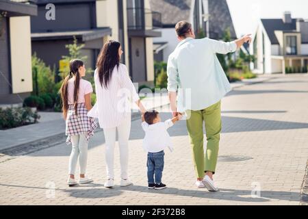 Foto sul retro di una bella famiglia ottimista a piedi tenere le mani vicino a casa indossare un panno casual all'esterno Foto Stock