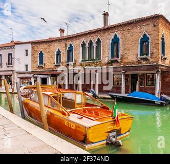 Canale e le sue barche, così come le facciate medievali dell'isola di Murano a Venezia in Veneto, Italia Foto Stock