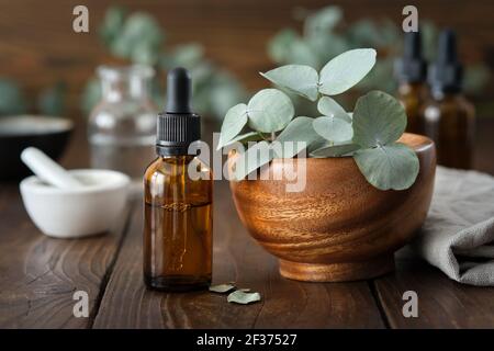 Flacone contagocce di olio essenziale di eucalipto e ciotola di legno di foglie di eucalipto verde. Mortaio e bottiglie di olio su sfondo, non in fuoco. Foto Stock