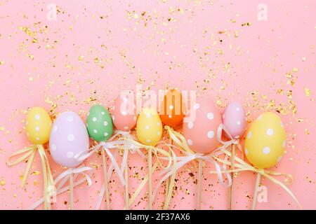 Uova di Pasqua colorate su bastoni su sfondo rosa con confetti dorati. Biglietto d'auguri per le festività pasquali Foto Stock