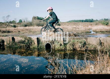 giovane ragazza sulla sua bici che cavalcano attraverso un grande puddle schizzi Foto Stock