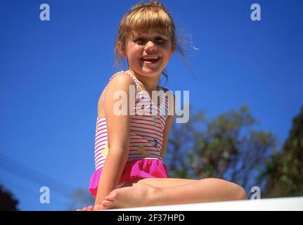 Giovane ragazza seduta su muro, Sumner, Christchurch, Canterbury Regione, Nuova Zelanda Foto Stock