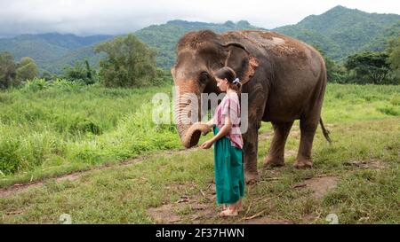 A nord di Chiang mai, Thailandia. Una ragazza sta accarezzando un elefante in un santuario per vecchi elefanti. Foto Stock