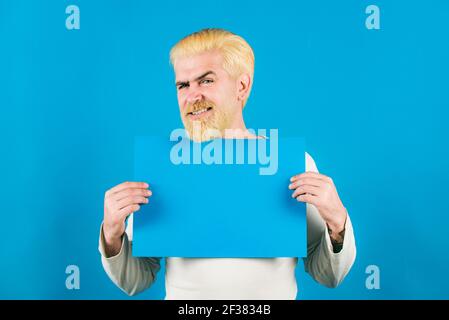 Ritratto dell'uomo che mostra un cartello blu vuoto con spazio di copia per slogan o testo. Il giovane mostra un foglio di carta nella macchina fotografica su un colore Foto Stock