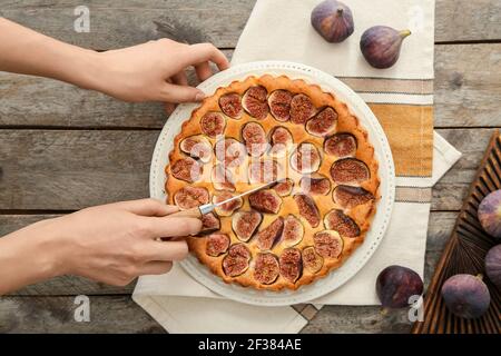 Donna che taglia deliziosa torta di fichi su sfondo di legno Foto Stock