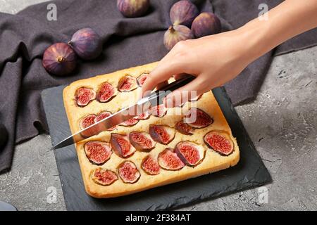 Donna che taglia deliziosa torta di fichi su sfondo grunge Foto Stock