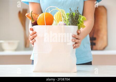 Donna e borsa di carta con diversi prodotti sul tavolo in cucina Foto Stock