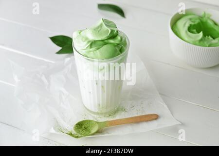 Bicchiere di gustoso latte di dalgona matcha e cucchiaio alla luce sfondo di legno Foto Stock