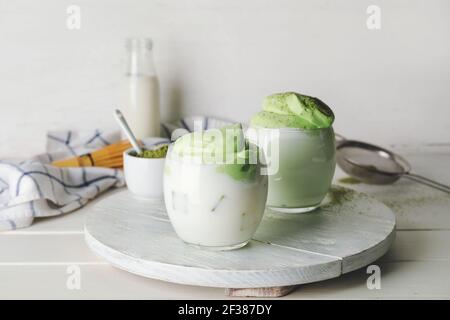 Vassoio con bicchieri di gustosa dalgona matcha latte e polvere su sfondo di legno chiaro Foto Stock