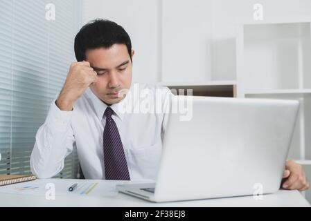 Uomo d'affari asiatico sempre stressato al lavoro di fronte al portatile computer - segnale acustico Foto Stock