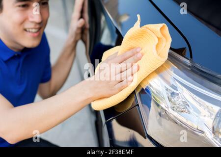 Un uomo che pulisce (pulendo) l'automobile con il panno di microfibra, il dettaglio dell'automobile o il concetto di valeting Foto Stock