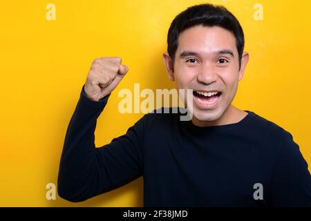 Giovane alzando il pugno con il viso felice sul giallo sfondo Foto Stock