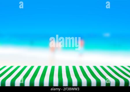 Tavolo coperto con tovaglia verde striato in sfocatura sfondo spiaggia - può essere utilizzato per la visualizzazione o il montaggio dei prodotti Foto Stock