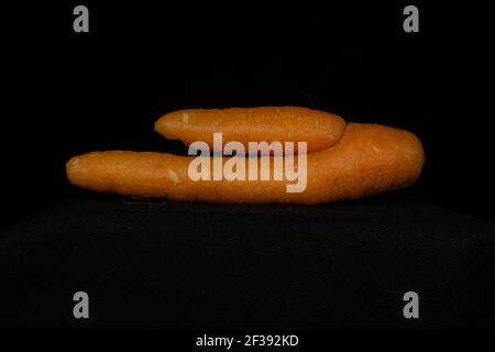 singola carota arancione deformata isolata su sfondo nero Foto Stock