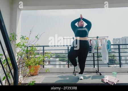 Concetto di salute, fitness e sport. Più la taglia giovane donna asiatica che fa l'esercitazione sul tappeto in balcone, andando perdere le libbre supplementari a casa, diventa forte a. Foto Stock