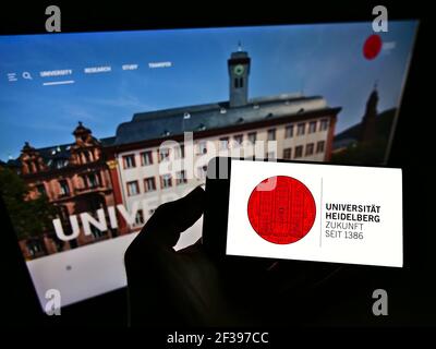 Persona che detiene il cellulare con il logo dell'università tedesca Ruprecht-Karls-Universität Heidelberg sullo schermo davanti alla pagina web. Mettere a fuoco il display del telefono. Foto Stock