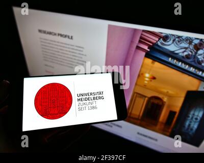 Persona che detiene smartphone con il logo dell'università tedesca Ruprecht-Karls-Universität Heidelberg sullo schermo davanti al sito web. Mettere a fuoco il display del telefono. Foto Stock