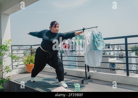 Concetto di salute, fitness e sport. Più la taglia giovane donna asiatica che fa l'esercitazione sul tappeto in balcone, andando perdere le libbre supplementari a casa, diventa forte a. Foto Stock