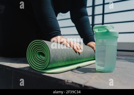 Primo piano di una mano femminile più dimensione è rotolare su tappetino di esercizio e si prepara a fare yoga. Lei si sta allenando sul tappetino del pavimento in balcon sole mattina Foto Stock