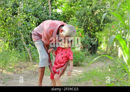 Nonno anziano di origine indiana che tiene amorevolmente il nipote più giovane, india. Concetto per i ricordi dell'Infanzia, sorride sul volto del bambino piccolo Foto Stock