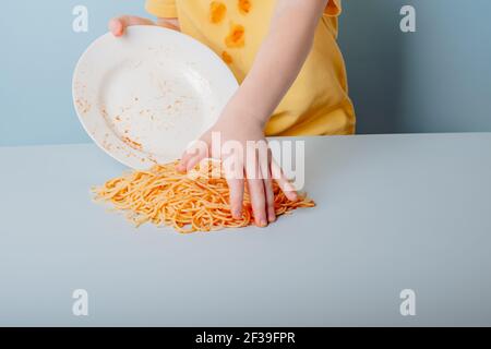 Bambino che mangia gli spaghetti con le mani, isolato su fondo blu. Foto di alta qualità Foto Stock