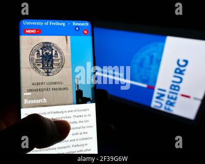 Persona che tiene il telefono cellulare con la pagina web dell'Università tedesca di Friburgo sullo schermo davanti al logo. Focus sul centro del display del cellulare. Foto Stock