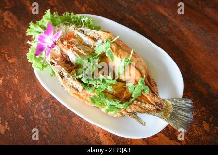 Pesce fritto con erbe e verdure, cibo cotto filetto di pesce di spigola sul piatto su tavola di legno Foto Stock